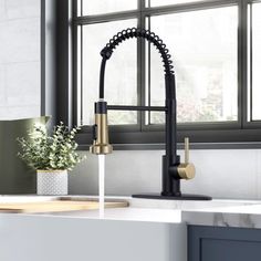 a kitchen sink with black faucet and gold handles in front of a window