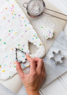 someone decorating a christmas tree shaped cake with icing and sprinkles