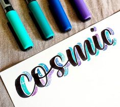 four different colored pens sitting on top of a white piece of paper with the word cosmic written in it