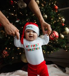 a baby wearing a santa hat standing in front of a christmas tree