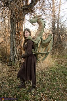 a woman dressed as a dragon poses in front of a tree