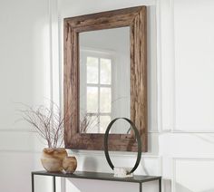 a wooden mirror sitting on top of a table next to a vase with flowers in it