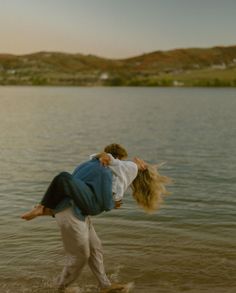 two people are walking in the water with their arms around each other and one is carrying another person