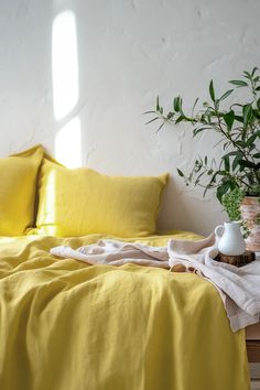 a bed with yellow linens and a potted plant