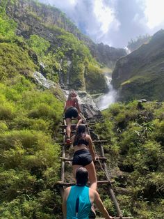 three people walking up stairs in front of a waterfall with water coming down the side