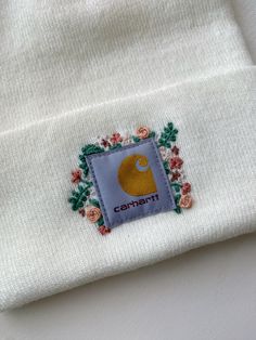 a white beanie with an embroidered patch on the front and side, sitting on top of a table