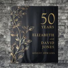 a black and gold 50th anniversary banner hanging from a brick wall with leaves on it