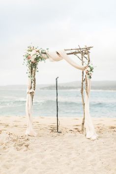 an outdoor wedding setup on the beach with flowers and ribbon draped over the arch,