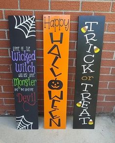 three wooden halloween signs sitting next to a brick wall