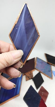 a person holding up a small piece of glass in front of some smaller pieces of tile