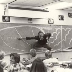 a man standing on top of a chalk board in front of a classroom full of people