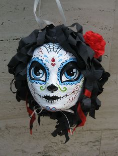 a white mask with blue eyes and red roses on the head is hanging from a hook