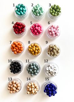 an assortment of different colored beads in small glass bowls on a white table with numbers