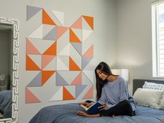 a woman sitting on her bed reading a book in front of a colorful wall art