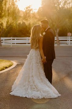 a bride and groom standing in front of a white fence with the sun behind them