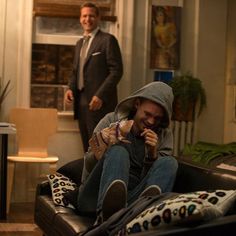 a man sitting on top of a couch next to another man in a living room