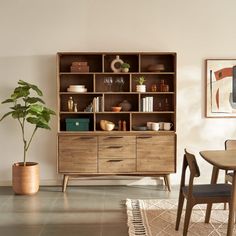 a dining room table with chairs and a book shelf in the corner next to a potted plant