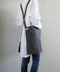 a man standing in front of a white wall wearing a gray apron and black suspenders