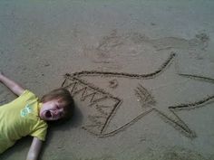 a little boy laying on the sand next to a star drawn in the sand with his hands