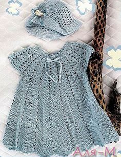 a crocheted blue dress and hat on a bed next to a stuffed animal