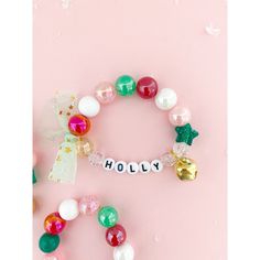 a bracelet with the word holly spelled out on it and christmas decorations around it in front of a pink background