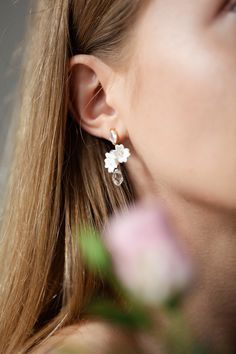 a close up of a person wearing some kind of earring with flowers in the background