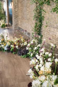 a bunch of flowers that are on the side of a brick wall and some plants