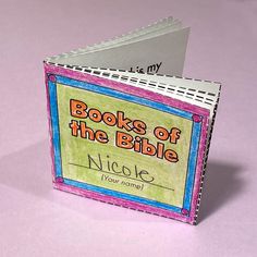 an open book with the words books of the bible written in pink and blue on it