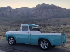 an old blue and white truck parked on the side of the road in front of mountains