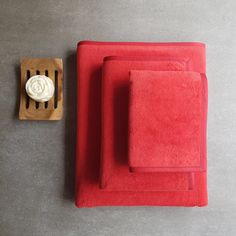 two red towels sitting next to each other on top of a gray floor with a wooden holder