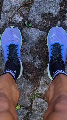 the feet of a person wearing blue and black running shoes, standing in front of some rocks