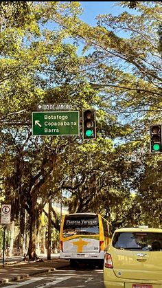 a yellow van driving down a street next to a traffic light and green signs on a tree lined street