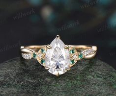 an engagement ring with a pear shaped diamond and emerald accents