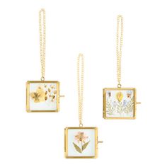 three square pendants with flowers on them hanging from chains, one in gold and the other in white