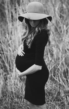 a pregnant woman wearing a hat poses for a black and white photo