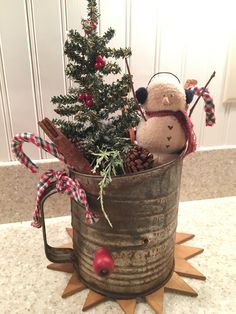 a small christmas tree in an old metal mug with a snowman decoration on top