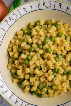 a bowl filled with pasta and peas on top of a table next to an onion