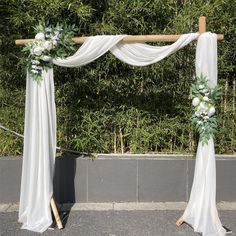 an outdoor wedding ceremony setup with white drapes and floral arrangements on the side walk