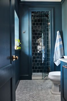 a bathroom with blue walls and tile flooring is pictured in this image, the shower door is open