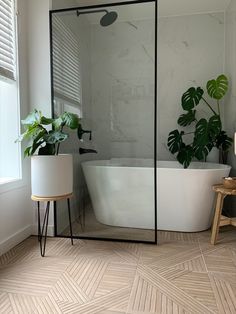 a white bath tub sitting next to a green plant in a bathroom under a window