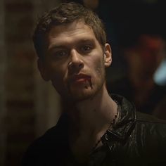 a man with blood on his face standing in front of a brick wall