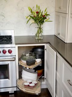 a kitchen with white cabinets and black counter tops, an open corner shelf holds pots and pans