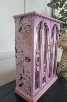 a purple cabinet with flowers painted on the front and sides, sitting on a table next to a potted plant