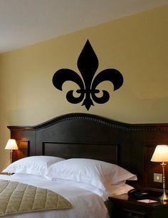 a bed room with a neatly made bed and a fleur de lis wall decal