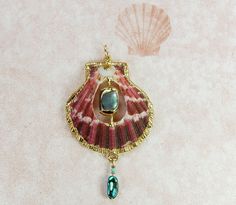 This a Royal Cloak scallop, named for its deep royal burgundy colors. The white, horizontal stripes add a nice contrast, too. A window has been cut in the shell so an accent stone of shimmering, blue/green paua shell could be added. Another polished paua shell and decorative beads suspends from the bottom of the shell. The accent trim is 18 kt electroformed gold. The pendant measures 1.70 inches in height. Carved Shell Jewelry, Shell Necklace, Royal Cloak, Ocean-inspired Beaded Gold Shell, Elegant Shell-shaped Brass Jewelry, Handmade Blue Shell-shaped Necklace, Ocean-inspired Abalone Shell Decor, Blue Ocean-inspired Shell-shaped Necklace, Ocean-inspired Blue Shell-shaped Necklace