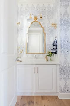 a white and gold bathroom with wallpaper on the walls, sink and vanity area