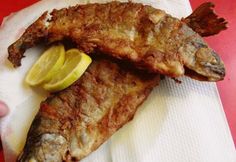 two pieces of fish on a napkin with lemon wedges