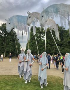 some people are standing in the grass with horses on their heads and holding long sticks