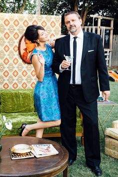 a man and woman standing next to each other in front of a table with food on it