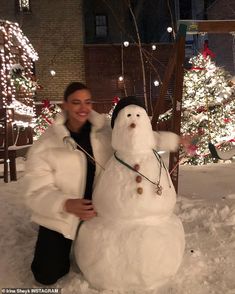 a woman standing next to a snowman in front of a christmas tree with lights